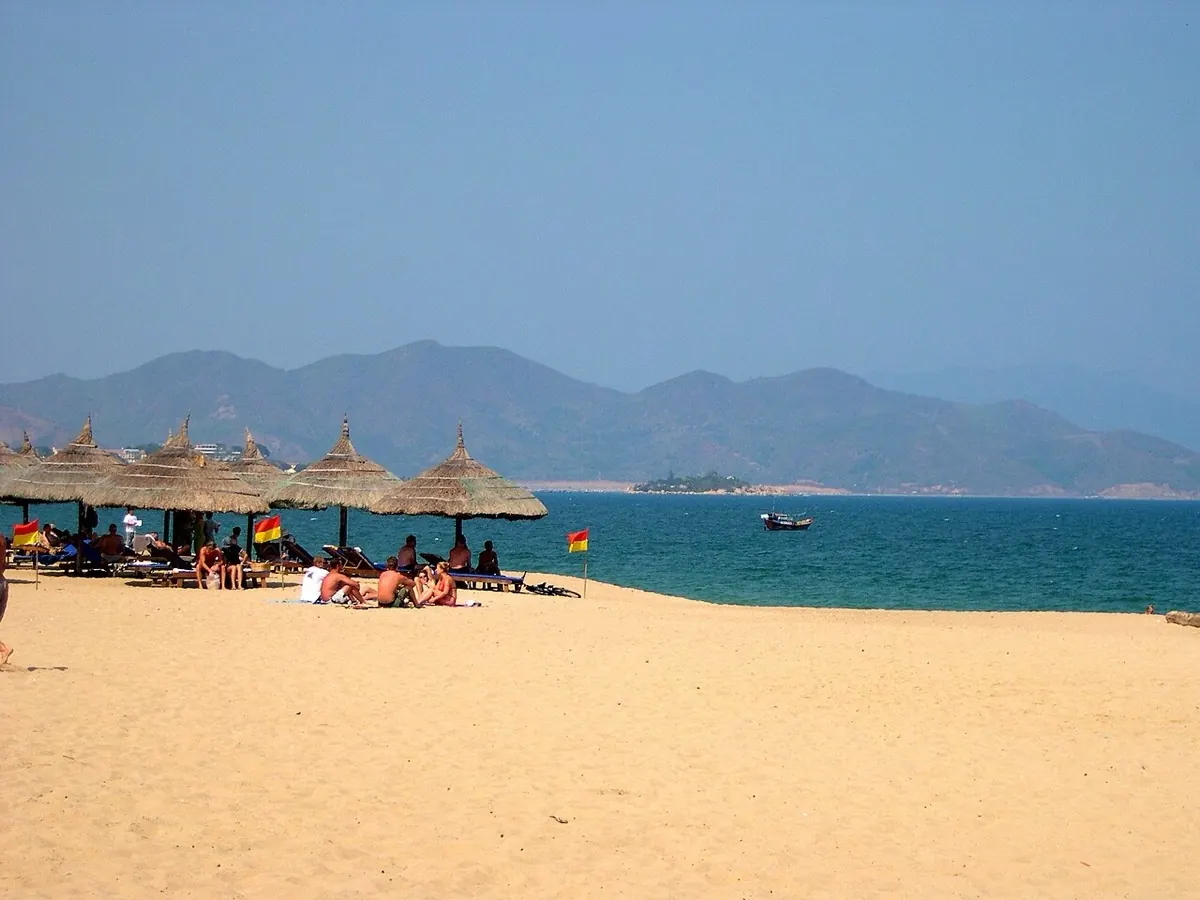 Bãi biển Nha Trang với dù lá, khách tắm nắng và dãy núi phía xa