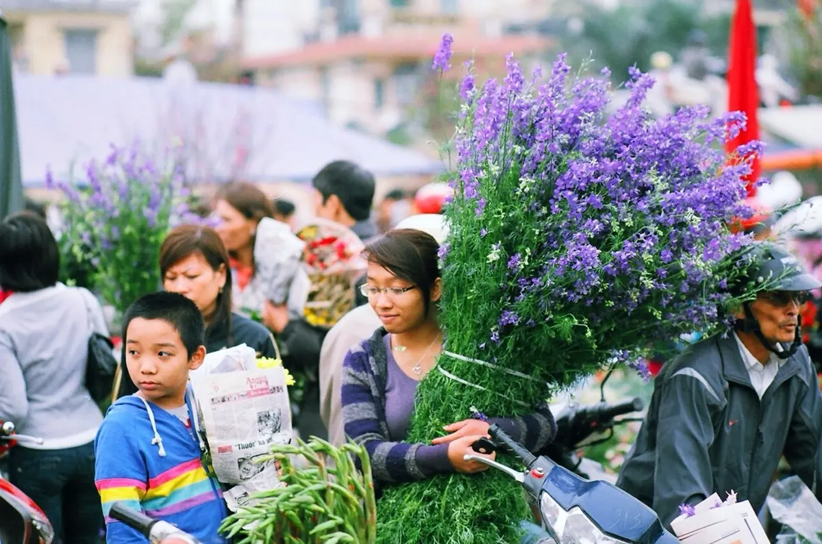 Người dân chen nhau mua hoa ở chợ hoa ngày Tết, một phụ nữ ôm bó hoa tím